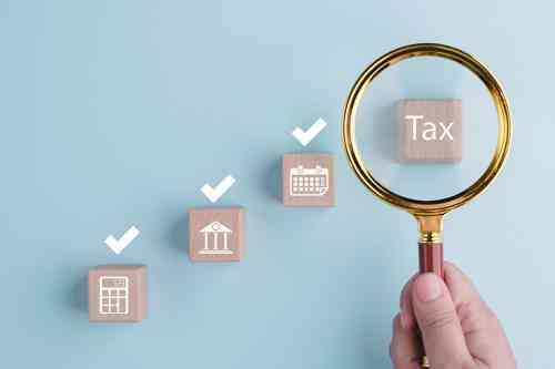 © Bussarin / stock.adobe.com Lupe vergrößert Holzklotz mit Aufschrift Tax